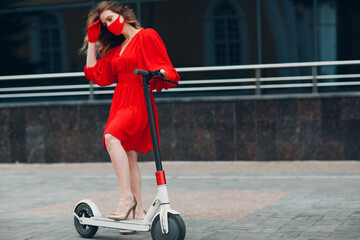 Young woman with electric scooter in red dress and gloves with medical face mask at the city.