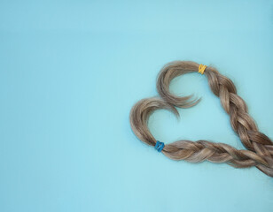 Curls of hair braided into a braid in the shape of a heart on a blue background. Copy space.