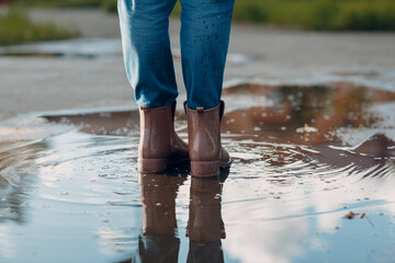 Woman wearing rain rubber boots walking running and jumping into puddle with water splash and drops in autumn rain.