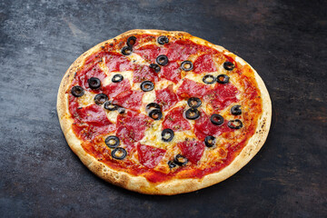 Traditionelle italienische Pizza al salame mit Salami, Mozzarella und Oliven serviert als close-up auf einem alten rustikalen Board mit Textfreiraum 