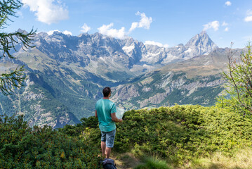Standing man holding a map and looking at Matterhorn from a lookout in italian alps. Active summer vacations. 
