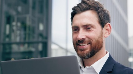 Close-up smiling successful businessman working on laptop outdoors joyful bearded male manager freelancer remotely communicating with client journalist writer writing article thinking about new idea