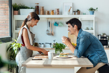 Happy young couple enjoying breakfast while talking in the kitchen at home.