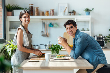 Happy young couple enjoying breakfast while talking in the kitchen at home.