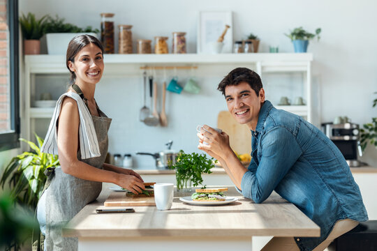 Happy young couple enjoying breakfast while talking in the kitchen at home. - Powered by Adobe