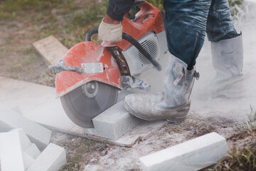 Worker mason cuts the sidewalk tile with circular saw while repairing sidewalk in city street.