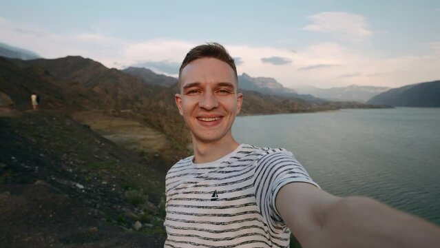 Young hiker traveler man taking selfie at mountain top. Action. Young happy man with mountains and beautiful lake on the background.