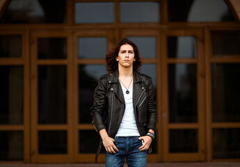 a young, handsome man with long dark hair, wearing a leather jacket, jeans and a white T-shirt,...