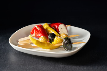 Finger food sticks with olives and stuffed pepperoni on white plate.
