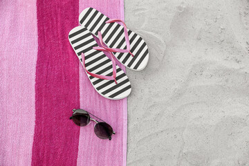 Towel with stylish flip flops and sunglasses on sand, flat lay. Space for text