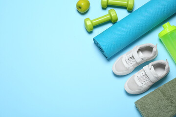 Exercise mat, dumbbells, apple, towel, shaker and shoes on light blue background, flat lay. Space...