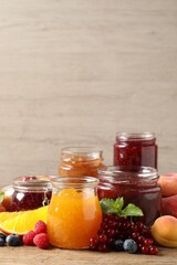 Fototapeta na wymiar Jars with different jams and fresh fruits on wooden table. Space for text