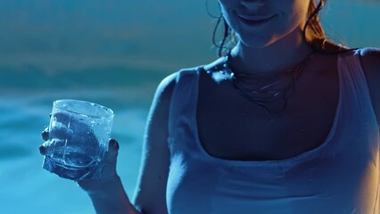 Wet sexy woman drinking alcohol and dancing in water in swimming pool at night. Summer party, body moving, lady in tight white dress. Night lifestyle, cocktails, entertainment for adults