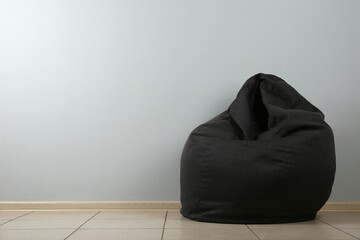 Black bean bag chair near light grey wall. Space for text