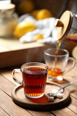Glass cup with delicious tea and sugar on wooden table, space for text