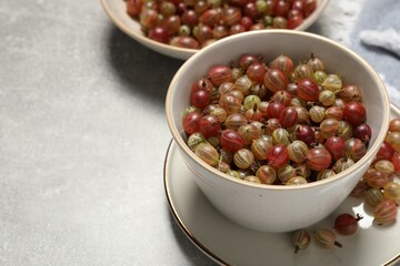 Fresh ripe gooseberries in bowls on light grey table. Space for text