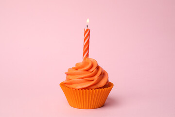 Delicious birthday cupcake with orange cream and burning candle on pink background