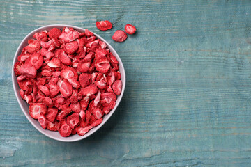 Bowl and dried strawberries on light blue wooden table, flat lay. Space for text