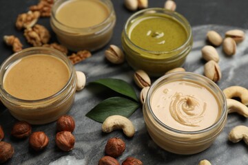 Jars with butters made of different nuts and ingredients on black table, closeup