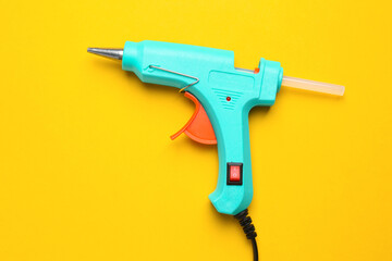 Turquoise glue gun with stick on yellow background, top view