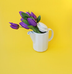 Teapot and purple tulips layout on a yellow background. Holiday greeting concept.