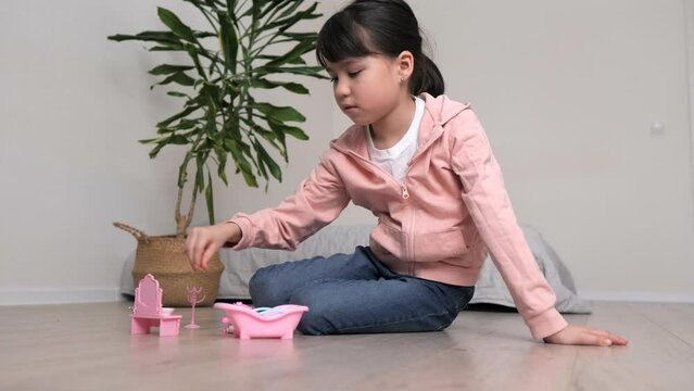 Cute little girl is playing with toys on the floor in white room. Kid have fun in her room. 
