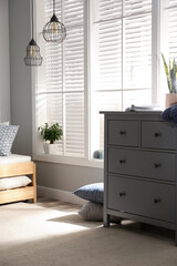 Grey chest of drawers near window in stylish bedroom interior
