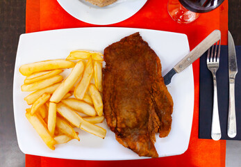 Breaded pork schnitzel in oven with fried potatoes served on table with cutlery and bread