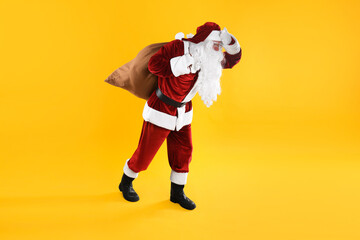 Fototapeta na wymiar Full length portrait of Santa Claus with sack on yellow background