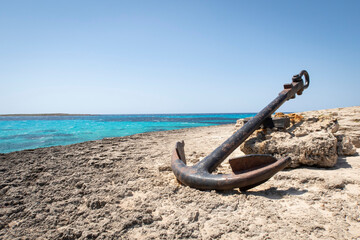 a large old anchor, stranded on a rocky cliff with a sea of turquoise water, copy space anchor of Punta Prima, Menorca, Spain  © Javier