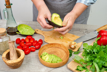 woman's hands preparing avocado to serve. Kitchen table with vegetables and spices