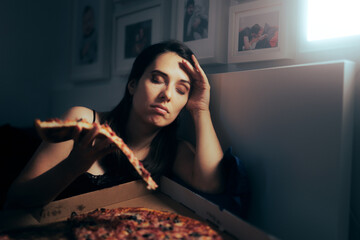 Stressed Tired Woman Having a Slice of Pizza at Night . Unhappy tired depressed person binge eating...