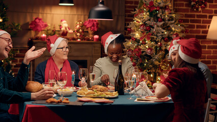Positive diverse people smiling heartily while enjoying Christmas dinner at home with loved ones. Happy family members celebrating winter feast with traditional home cooked food. Handheld shot