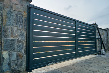 Wide automatic sliding gate with remote control installed in high stone fense wall. Security and...