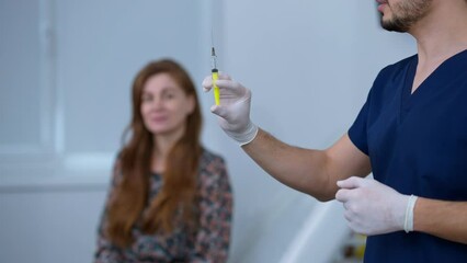 Unrecognizable doctor preparing syringe with facelift injection standing on the right with blurred woman waiting at background. Confident professional Middle Eastern man and Caucasian woman indoors