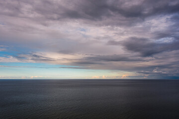 A beautiful cloudy sky with hints of an upcoming sunset over the sea, where the breeze creates waves like ripples on a summer evening.
