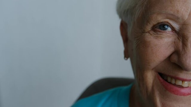 Close up portrait of beautiful older woman smiling and standing by wall with gray eyes.