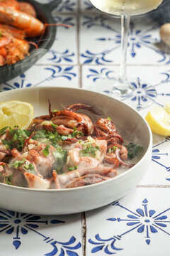 grilled squid with garlic and lemon juice, parsley, a glass of white wine, on a background of natural ceramic tiles with a Mediterranean ornament