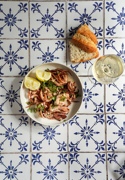 squid fried with garlic and lemon juice, parsley, a glass of white wine, on a background of natural ceramic tiles with a Mediterranean ornament