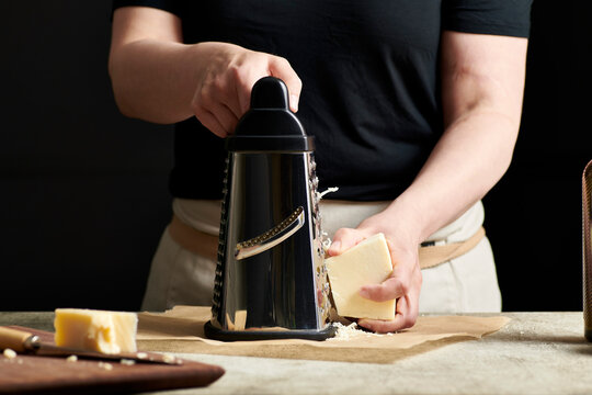 Hands grating cheese onto parchment paper.