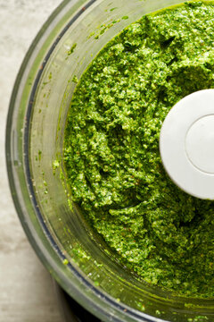 Bright green pesto in the bowl of a food processor.