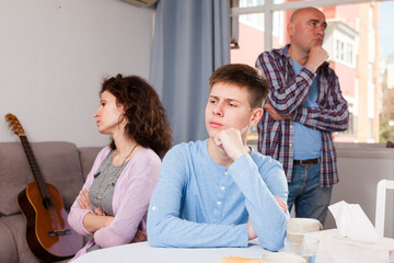 Portrait of upset teenage boy and his frustrated parents in home interior looking away after quarrel