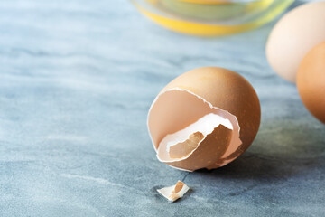 A cracked eggshell with two whole eggs and an egg yolk in a glass bowl.