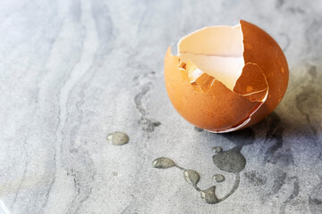 A cracked eggshell with eggwhite on a marble surface.