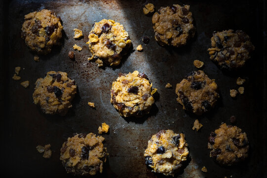 Corn flake and date cookies on a baking tray in light and shadow.