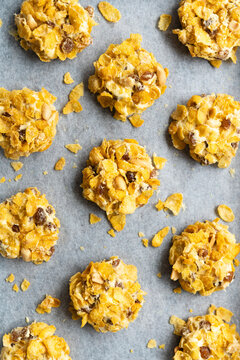 Cornflake, peanut and sultana cookies on a baking tray.