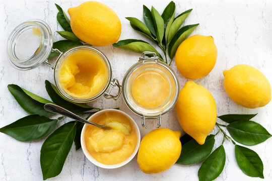 Lemon curd in jars and a bowl amongst whole lemons and leaves.