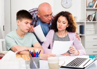 Young man with his wife and teen son reading documents at home table