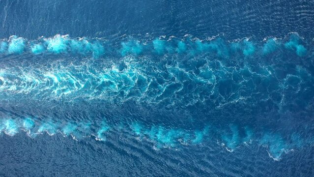 Wake of a cargo ship texture on the sea surface. Engine roars at full speed and leaves wake water on the Ocean. Aerial top down view of water foam trace behind the tanker
