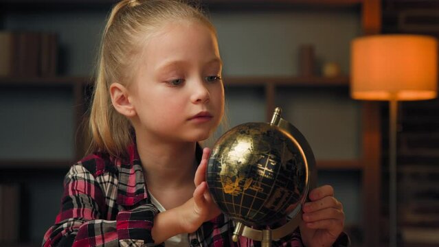 Female junior child schoolgirl pretty pupil looking and spinning colorful globe in study room exploring world search countries on global map of planet learning dreaming about future holidays abroad